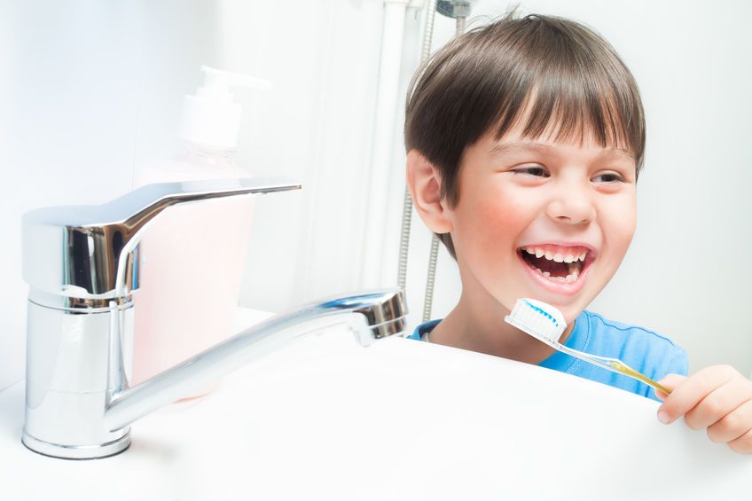 Laughing young boy holding toothbrush in front of bathroom sink