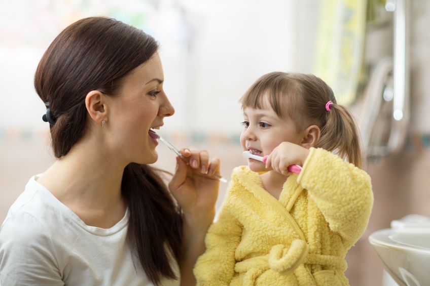 Stylish young mother showing infant girl how to brush teeth