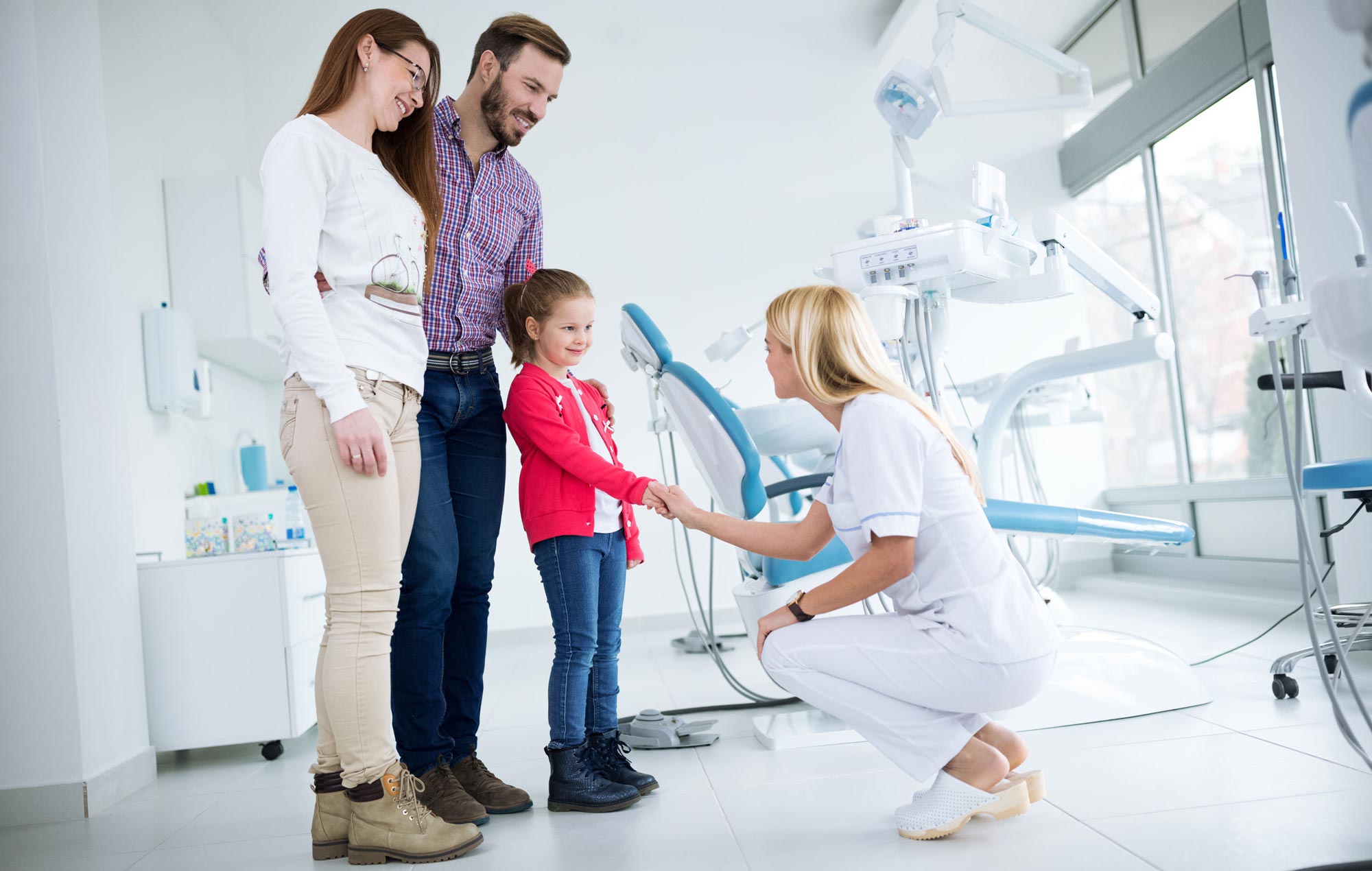 Crouching dental hygienist shaking hands with child in front of smiling parents