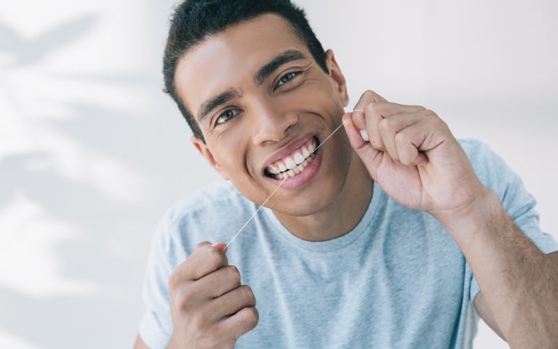 young man using dental floss looking camera
