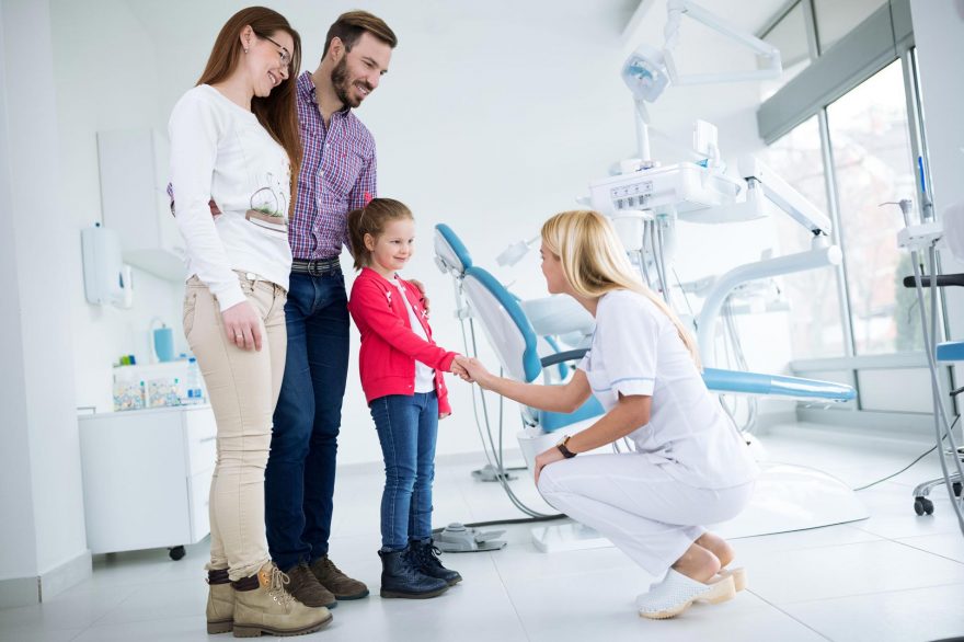 Crouching dental hygienist shaking hands with child in front of smiling parents