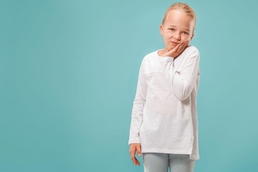 Frowning young girl applying pressure to cheek with toothache