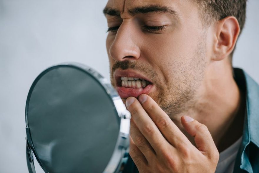 Man with toothache inspecting teeth in mirror