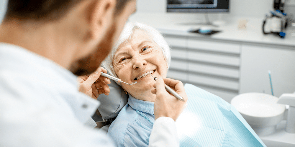 Stoney Creek dentist inspecting happy elderly patient's dentures with dental tools