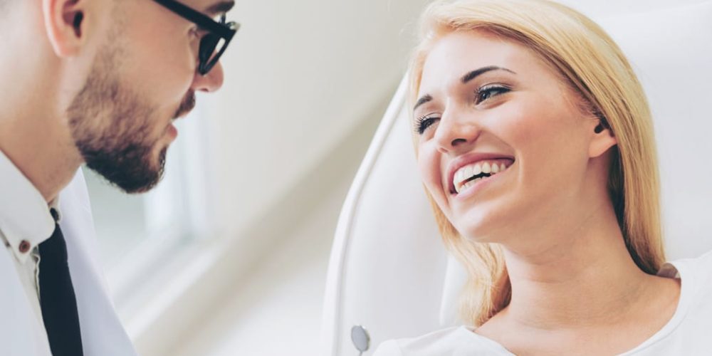 Bearded dentist with glasses conversing with seated female patient in Stoney Creek dental office