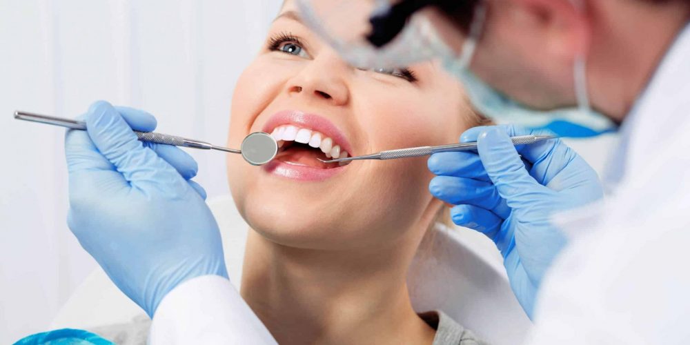 Stoney Creek dentist examining young woman's mouth with mirror and plaque scraper