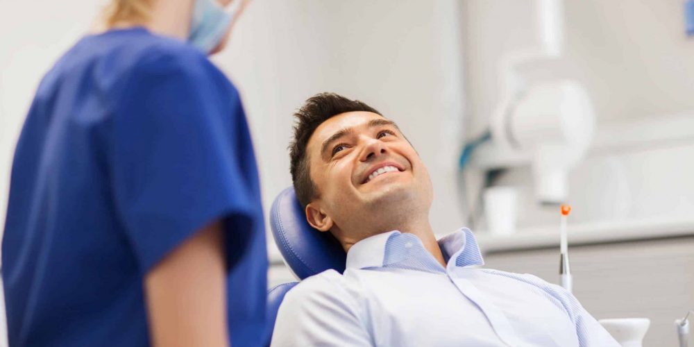 Professional dental hygienist smiling with seated male patient in Stoney Creek dental office