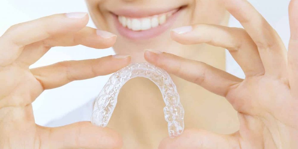 Confident young woman holding up clear Invisalign aligner with both hands